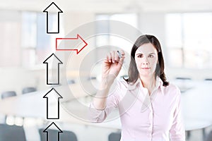 Businesswoman drawing arrows in different directions. Office background.