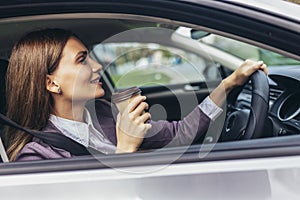Businesswoman driving in a car to work during the day, drink coffee. Steering wheel on the right side of the car