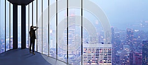 Businesswoman in empty office looking out of panoramic window with bright city downtown and sky view with mock up place. Future,