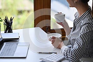 Businesswoman enjoy coffee break and looking out of the office window.