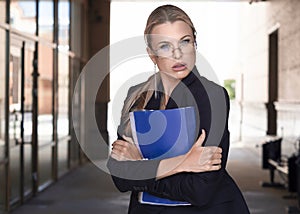 Businesswoman in eyeglasses tightly holds a folder with important documents and incredulously looks at the camera.