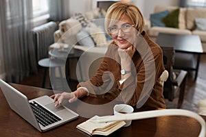 Businesswoman. Female Uses Laptop. Mature Woman Remote Homework Concept. Older Model in Brown Jacket And Eyeglasses.