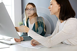 Businesswoman giving presentation to her female colleague while they sitting at the desk with computer. Group of