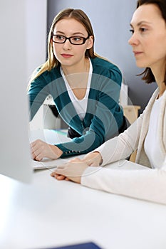 Businesswoman giving presentation to her female colleague while they sitting at the desk with computer. Group of