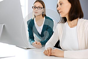 Businesswoman giving presentation to her female colleague while they sitting at the desk with computer. Group of