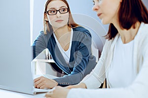 Businesswoman giving presentation to her female colleague while they sitting at the desk with computer. Group of