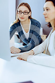 Businesswoman giving presentation to her female colleague while they sitting at the desk with computer. Group of