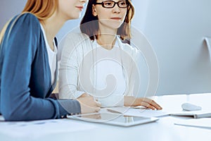 Businesswoman giving presentation to her female colleague while they sitting at the desk with computer. Group of