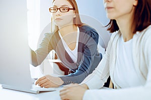 Businesswoman giving presentation to her female colleague while they sitting at the desk with computer. Group of