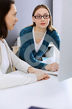 Businesswoman giving presentation to her female colleague while they sitting at the desk with computer. Group of