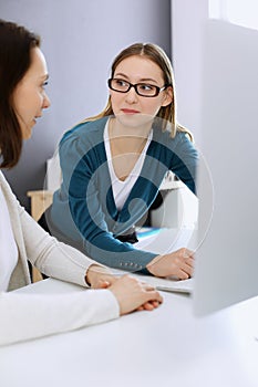 Businesswoman giving presentation to her female colleague while they sitting at the desk with computer. Group of