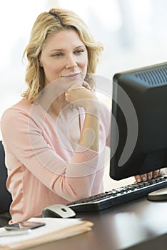 Businesswoman With Hand On Chin Looking At Computer In Office