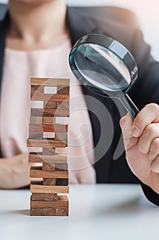 Businesswoman hand holding glass magnifying over wooden blocks tower. Business analysis, Risk Management, Study, opportunities and