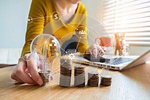 Businesswoman hand holding lightbulb with using calculator and laptop computer and money stack in office.