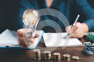 Businesswoman hand holding lightbulb with using calculator to calculate and money stack. Save energy and money with accounting