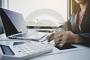 Businesswoman hand holding pen, analysis the graph with calculartor and laptop at the home office for setting challenging business