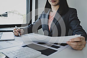 Businesswoman hand holding pen, analysis the graph with calculartor and laptop at the home office for setting challenging business