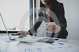 Businesswoman hand holding smartphone, analysis the graph with calculartor and laptop at the home office for setting challenging