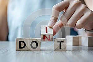 Businesswoman hand holding wooden cube with flip over block DON T to DO IT word on table background. success, strategy, solution,