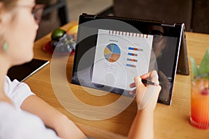 Businesswoman hand pointing with stylus on the chart over convertible laptop screen in tent mode. Woman using 2 in 1 photo