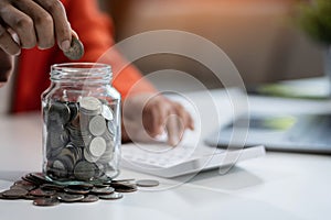 businesswoman hand puting coins in glass for saving money. concept finance and accounting in the home
