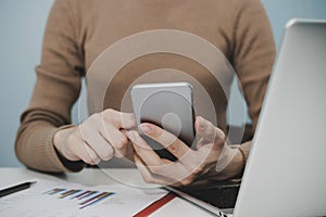 Businesswoman hand working with digital mobile smartphone, laptop computer and report on desk