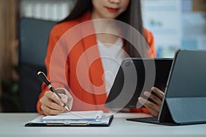 Businesswoman hand working at a tablet, computer and writing on a notepad with a pen in the office. on the wooden desk there a