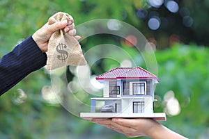 Businesswoman handed the money in bag to woman holding model house and car on natural green background, New home and Real estate