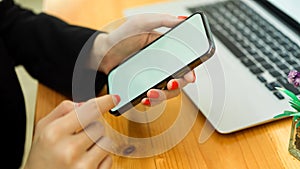 Businesswoman hands using smartphone on wooden table with laptop