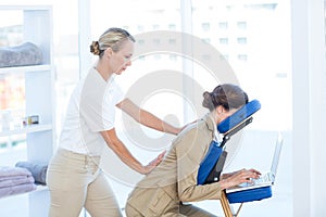 Businesswoman having back massage while using her laptop