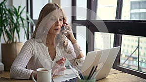 Businesswoman having mobile call in front of laptop screen at table in home office.