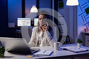 Businesswoman having phone call in start-up office late at night working at marketing project