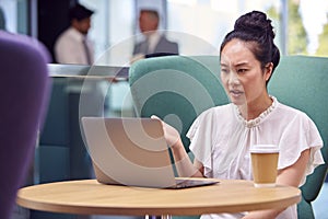 Businesswoman Having Video Call On Laptop At Table In Breakout Seating Area Of Office Building 