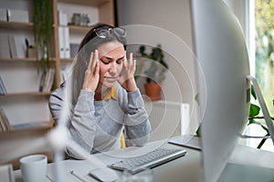 Businesswoman with headache at the desk indoors in office, feeling pain.