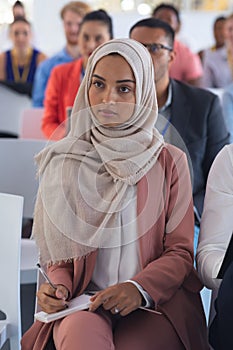 Businesswoman in hijab listening to speaker in a business seminar