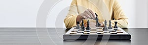 A businesswoman holding a black chess piece walks forward on a chessboard, comparing the chessboard to business administration.