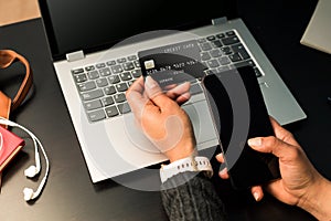 Businesswoman holding a black credit card and using the phone for make transactions online with the laptop. Concept teleworking