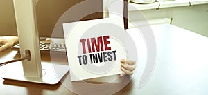 Businesswoman holding a card with text TIME TO INVEST, business concept