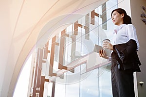 Businesswoman holding coffee and digital tablet outside office b