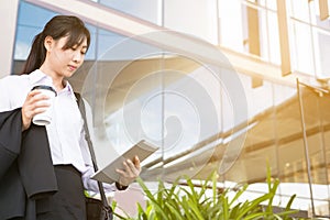 Businesswoman holding coffee and digital tablet outside office b