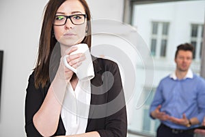 Businesswoman Holding Coffee Mug While Colleague Standing In Bac