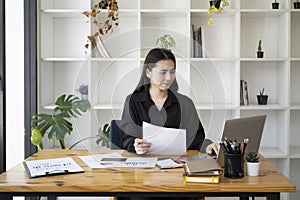 Businesswoman holding document and working with laptop at her office desk.