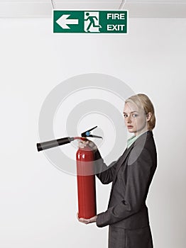 Businesswoman Holding Fire Extinguisher Under Exit Sign
