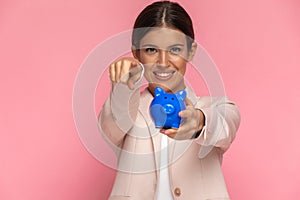 Businesswoman holding her piggy bank and pointing at the camera