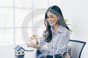 Businesswoman holding a house model .House on Hand with piggy bank.Real estate,Property insurance and security concept.Savings and