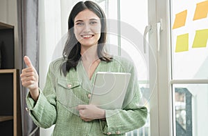 businesswoman holding laptop and showing thumbs up, Beautiful young woman using a tablet in the office