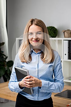 Businesswoman Holding Large File. young womanl standing in the office and holding folder. Portrait of young office worker holding