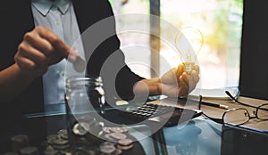 Businesswoman holding a light bulb while putting coin into a glass jar