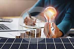 businesswoman holding light bulb with turbine on coins and solar panel. concept saving energy and finance accounting