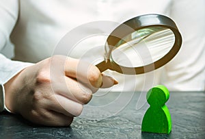 Businesswoman is holding a magnifying glass over a green man figure. Search for a talented employee. Identifying strengths in the